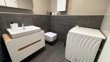A modern bathroom with a white sink, toilet, and washing machine.