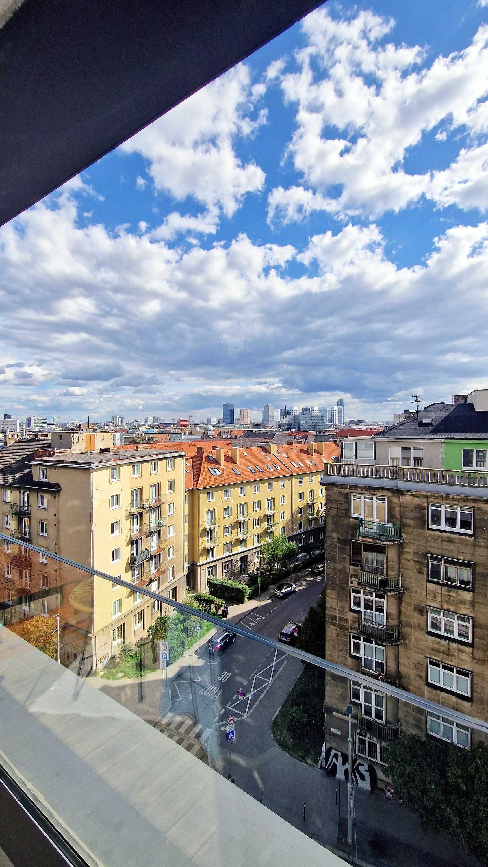En stadsbild med höga byggnader, en klar himmel med moln och en väg med fordon.