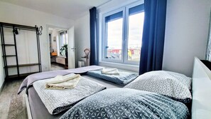 Ein Schlafzimmer mit zwei Betten, einem Fenster mit Vorhängen, einem Schreibtisch und einem Stuhl.