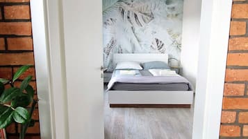 A bedroom with a bed, a nightstand, a potted plant, and a brick wall.