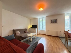 Ein möbliertes Wohnzimmer mit einer Couch, einem Tisch, einem Fernseher und einem Fenster.