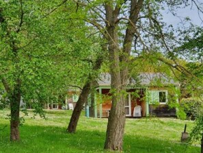 A rustic house with a front porch, surrounded by lush green trees and grass. - Family chalet with terrace - 6 guests (Baudreix)