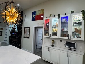 A modern kitchen with white cabinets, a marble countertop, and a Texas flag decoration. - Texas Oasis Retreat Near the Coast (Bay City)