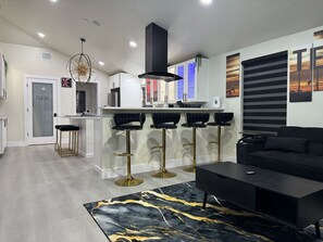 A modern kitchen with a central island, bar stools, and a black sofa in the living area. - Texas Oasis Retreat Near the Coast (Bay City)