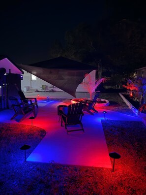 An outdoor seating area with chairs and a table under a large canopy, surrounded by a garden with decorative lighting. - Texas Oasis Retreat Near the Coast (Bay City)