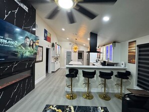 Una cocina moderna con una isla central, taburetes de bar y un televisor montado en la pared.