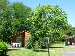 Eine Holzblockhütte mit Veranda und Sitzgelegenheit im Freien, umgeben von üppiger Vegetation und Bäumen.