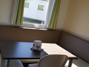 A small room with a single table and a chair, a window with curtains, and a view of a building outside. - Mobile home with terrace - 2 guests (Baudreix)