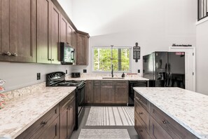 A modern kitchen with dark wood cabinets, a stainless steel refrigerator, and a large window with blinds. - 3 bedrm house nestled on 5 acres in Sevierville w/hot tub, private walking trail (Sevierville)