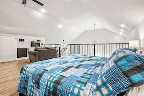 Un dormitorio con cama, una silla, un escritorio y un cuadro en la pared.