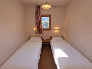 A small, single-room accommodation with two single beds, a window with a view, and a hanging light fixture. - Apartment, pets OK, parking - mountain view (Plagne Soleil)