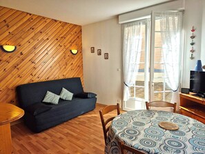 A cozy living room with a dark sofa, wooden flooring, a patterned table, and a TV on a wooden stand. - Apartment mountain view, terrace - 4 guests (Cauterets)