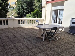 Un espace patio avec une table ronde et des chaises, une balustrade blanche et un bâtiment en arrière-plan.