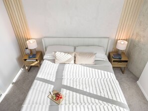 Ein ordentlich bezogenes Bett mit weißer Decke und Kissen, zwei Nachttische mit Lampen, ein kleiner Holzbeistelltisch und eine Obstschale auf dem Bett.