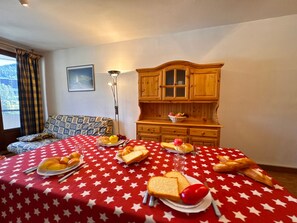 Zona pranzo con tavolo apparecchiato per la colazione, un divano, una lampada e pensili in legno.