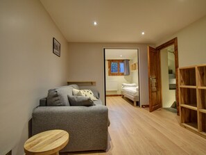 A compact bedroom with a grey sofa, a small wooden table, and a wooden wardrobe. - Family chalet in Morzine - 8 guests (Morzine)