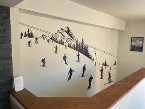 A wall with a ski slope mural, a wooden staircase, and a small white device on the wall. - Family chalet in Morzine - 8 guests (Morzine)