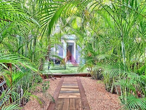 A wooden pathway leading to a building with a door, surrounded by dense tropical foliage. - Duplex house with air conditioning - 6 guests (Saint-Martin)