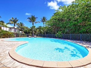 A swimming pool with a curved edge, surrounded by a stone deck and a metal fence. - Duplex house with air conditioning - 6 guests (Saint-Martin)