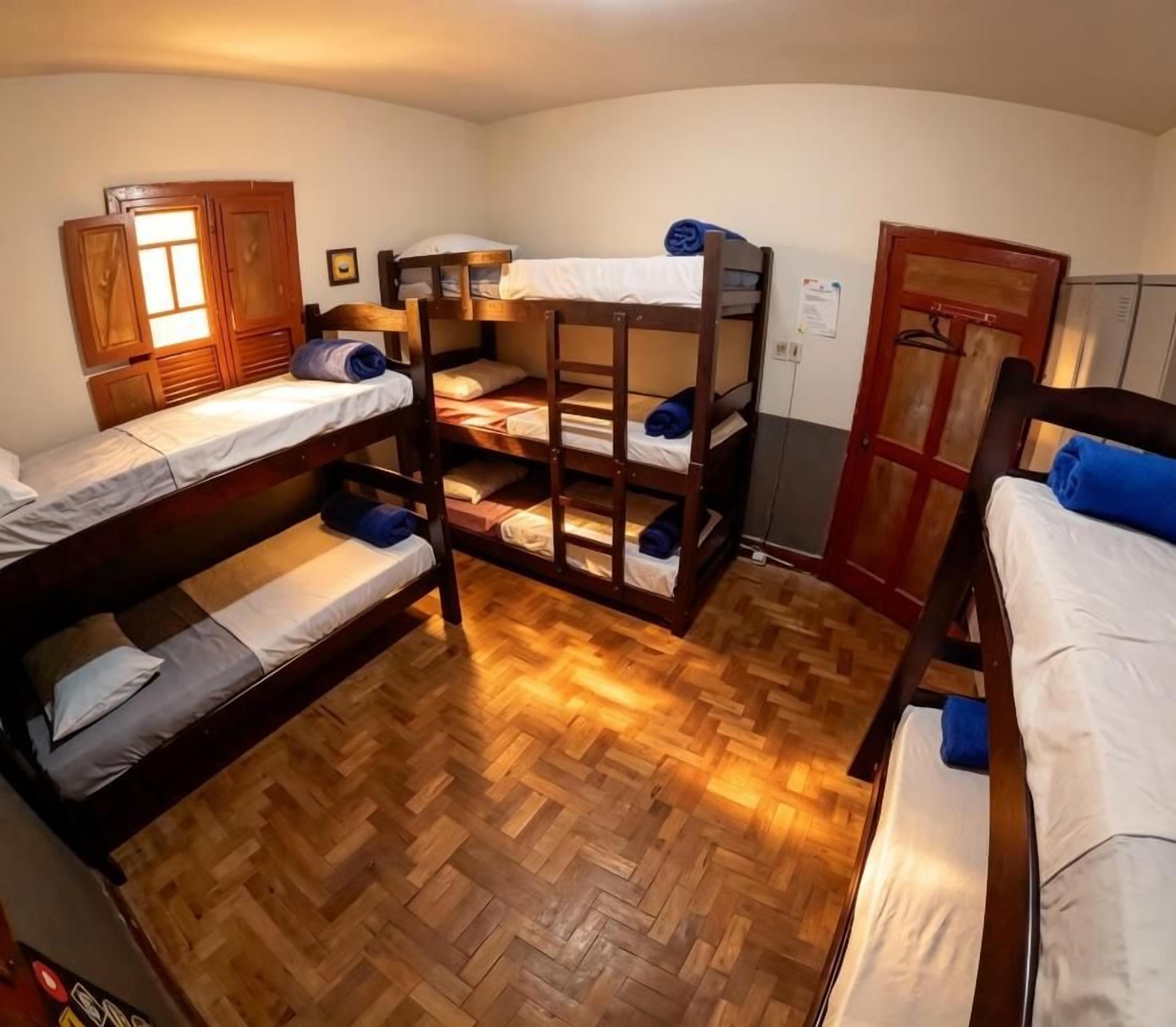 A dormitory room with bunk beds, wooden flooring, and a wardrobe.