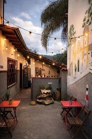 An outdoor patio with tables and chairs, a small fountain, and string lights. - Nuh Hostel (Ouro Preto)
