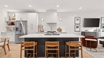 A modern kitchen with a central island, bar stools, a refrigerator, and a flat-screen TV.