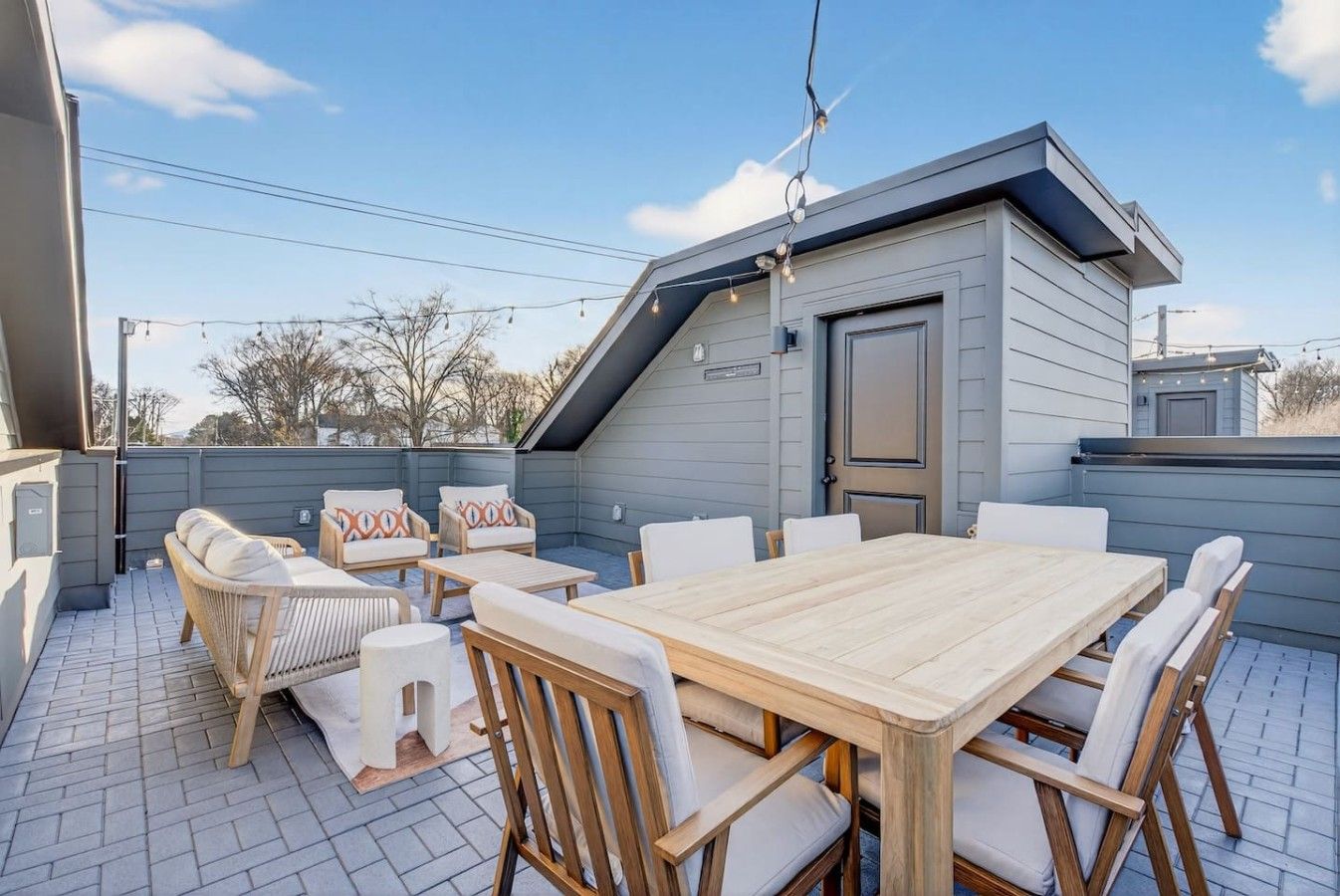 A covered patio with a wooden table and chairs, a small building, and a clear sky.