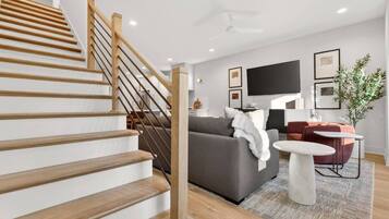 A modern living room with a staircase, a grey sofa, a coffee table, and a flat-screen TV.