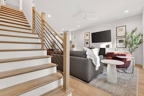 A modern living room with a staircase, a grey sofa, a coffee table, and a flat-screen TV. - Rooftop Patio, 3 Miles to Downtown + Walk to Restaurants (Nashville)