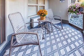 Un patio con dos sillas de mimbre, una mesita redonda y una planta en maceta con flores anaranjadas.