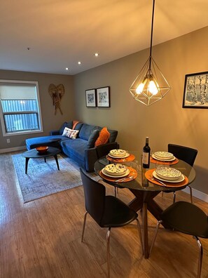 A dining area with a table set for four, a sofa in the background, and a hanging light fixture. - Ski-in/Ski-out 1Bdrm Luxury Condo, Slps 4, 1st fl, The Aspens, Pool & hot tubs (Whistler)