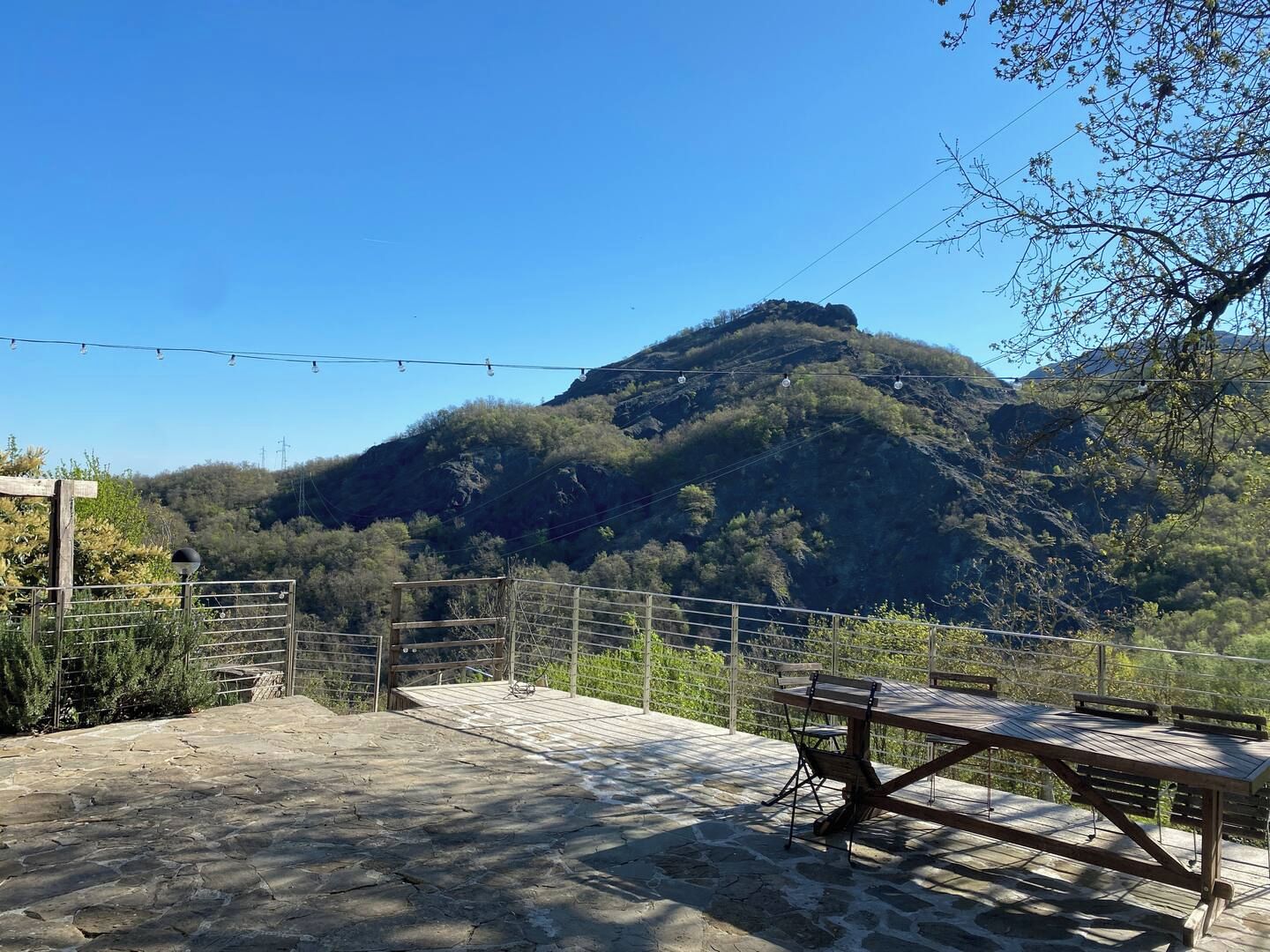 Un patio de piedra con una mesa y sillas de madera, con vistas a un paisaje montañoso.
