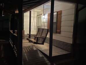 A wooden swing chair suspended from a ceiling, a wooden deck, and a building exterior with siding and a window. - Tranquil Nature Retreat in Denison, TX (Denison)