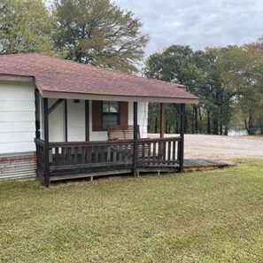 A single-story building with a porch, a small deck, and a grassy yard. - Tranquil Nature Retreat in Denison, TX (Denison)