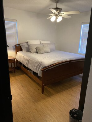 A bedroom with a wooden bed, white bedding, a ceiling fan, and a window with blinds. - Tranquil Nature Retreat in Denison, TX (Denison)