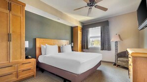 A hotel room with a large bed, wooden wardrobe, a desk, a chair, a ceiling fan, and a window with curtains. - Hilton Vacation Club Lake Tahoe Resort - 1BR Deluxe Near Heavenly (South Lake Tahoe)