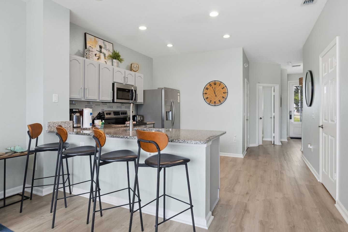 A modern kitchen with a central island, bar stools, and a clock on the wall.