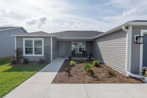 A residential house with a front porch, a small garden, and a visible garage door. - FREE GOLF CART!! IN The Heart Of the Southern Villages (Okahumpka)