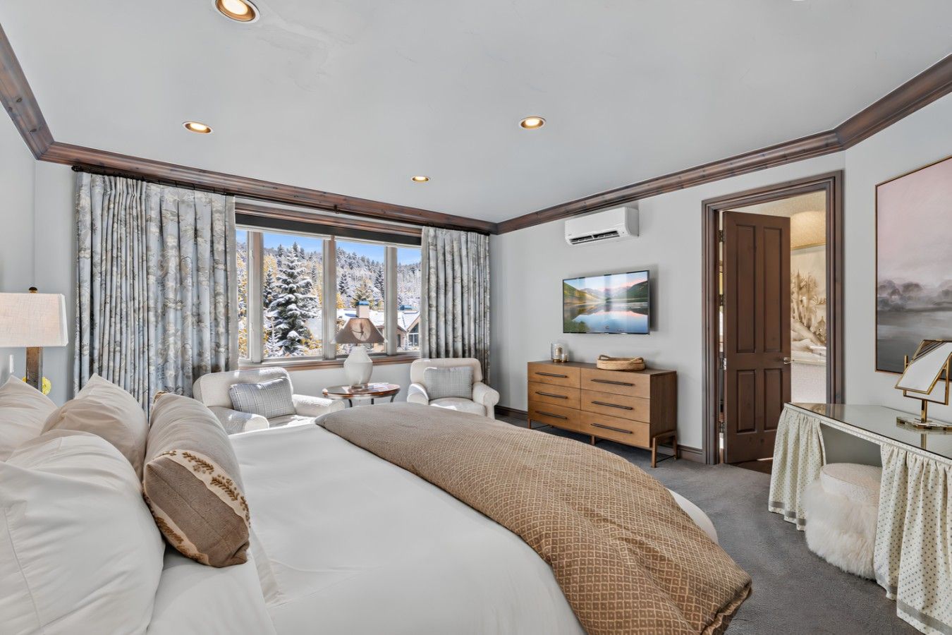 A bedroom with a large bed, a desk, a chair, a dresser, and a TV on the wall.