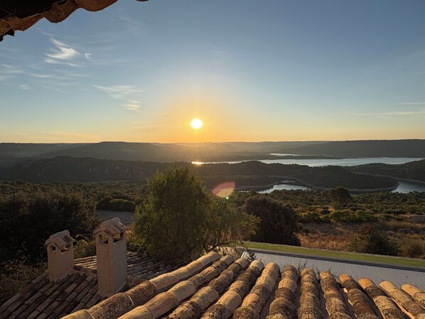 A sunset view from a terracotta-tiled roof overlooking a valley with a body of water and distant hills.