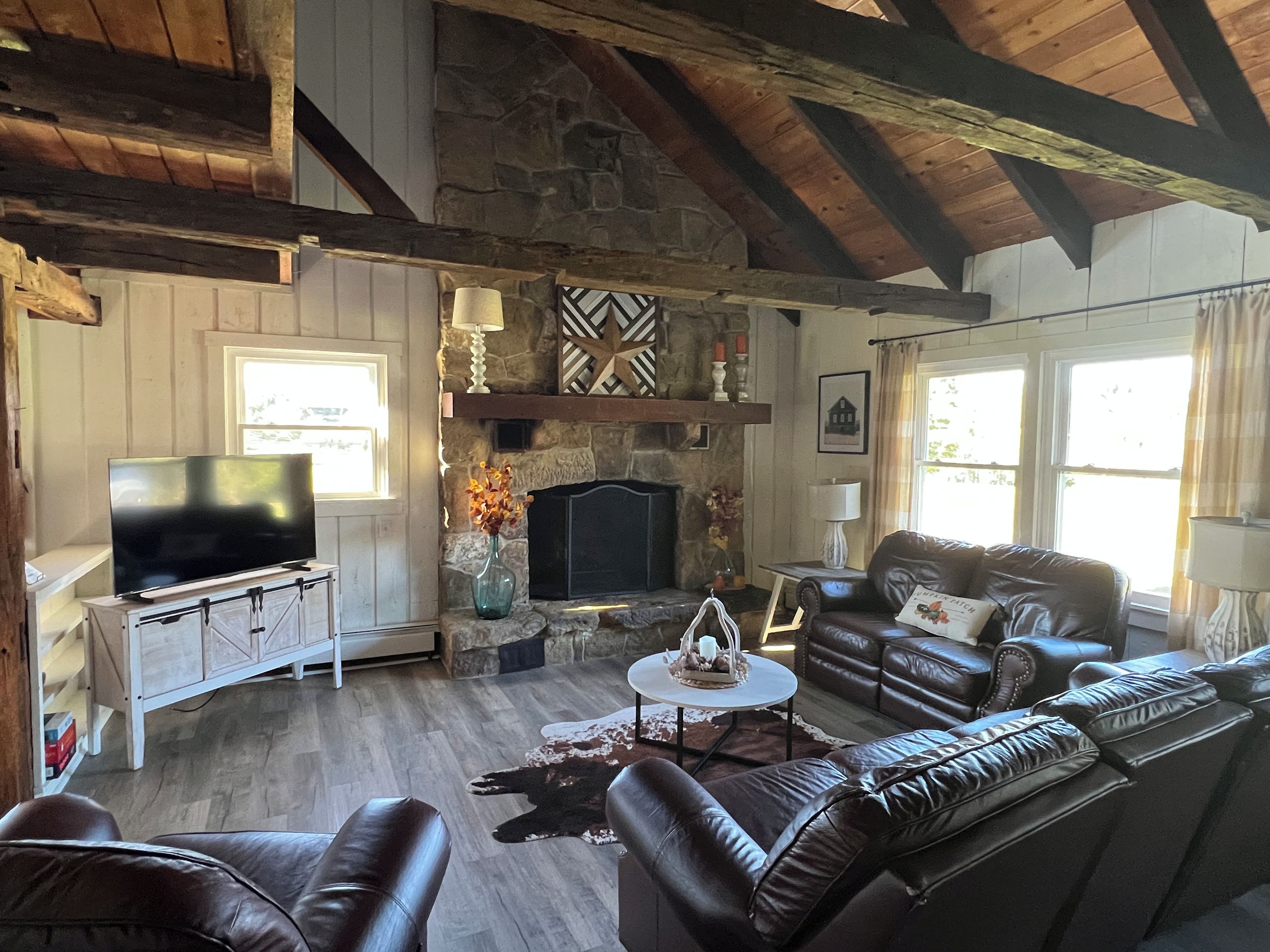 Ein gemütliches Wohnzimmer mit Kamin aus Stein, Ledersofas, einem Flachbildfernseher und einer rustikalen Decke.