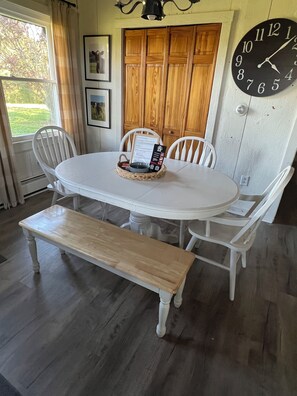 Un coin repas avec une table ronde, des chaises blanches, un banc, une horloge et des meubles en bois.