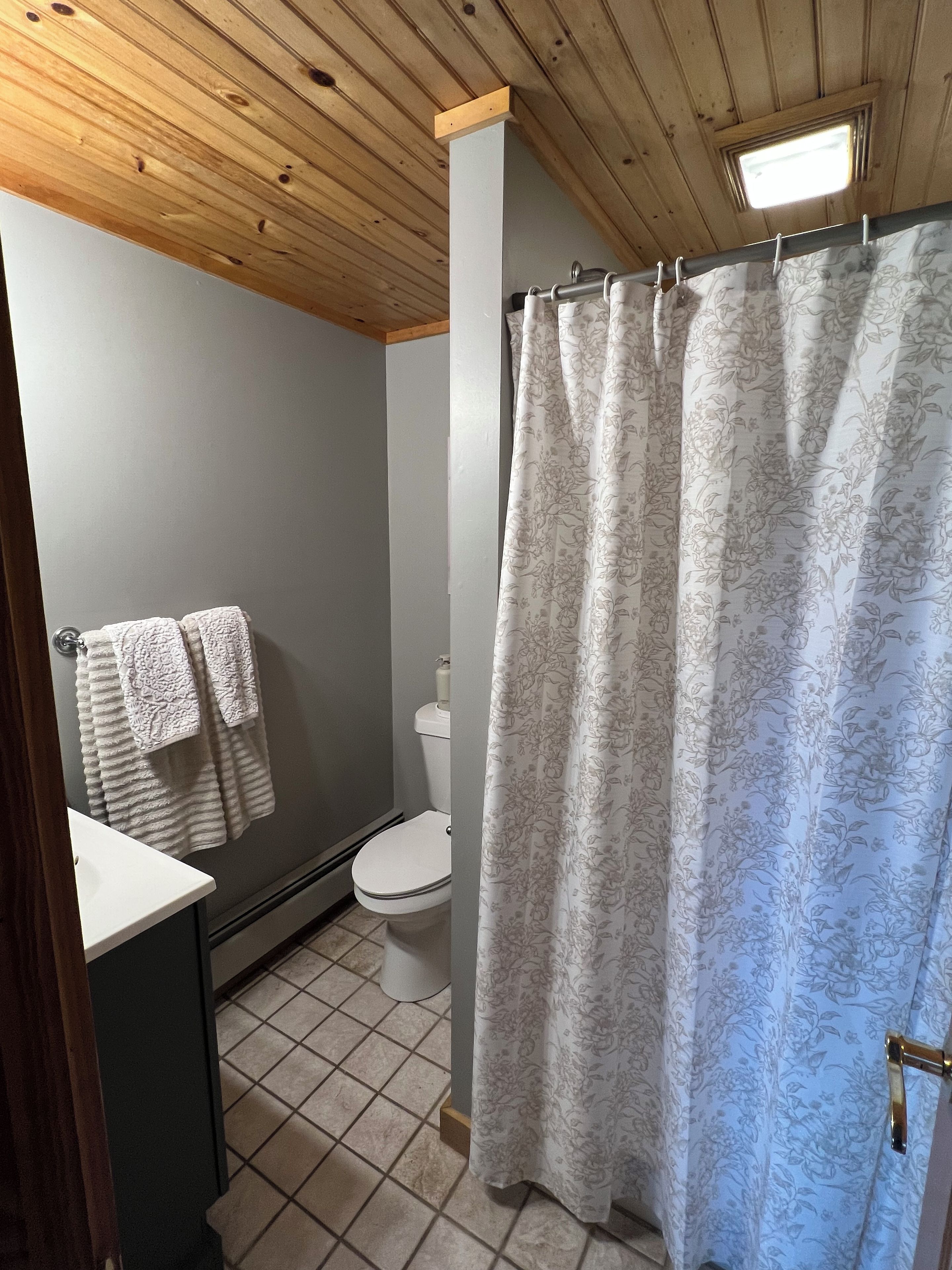 Un baño con inodoro, lavamanos, cortina de ducha y toallero.