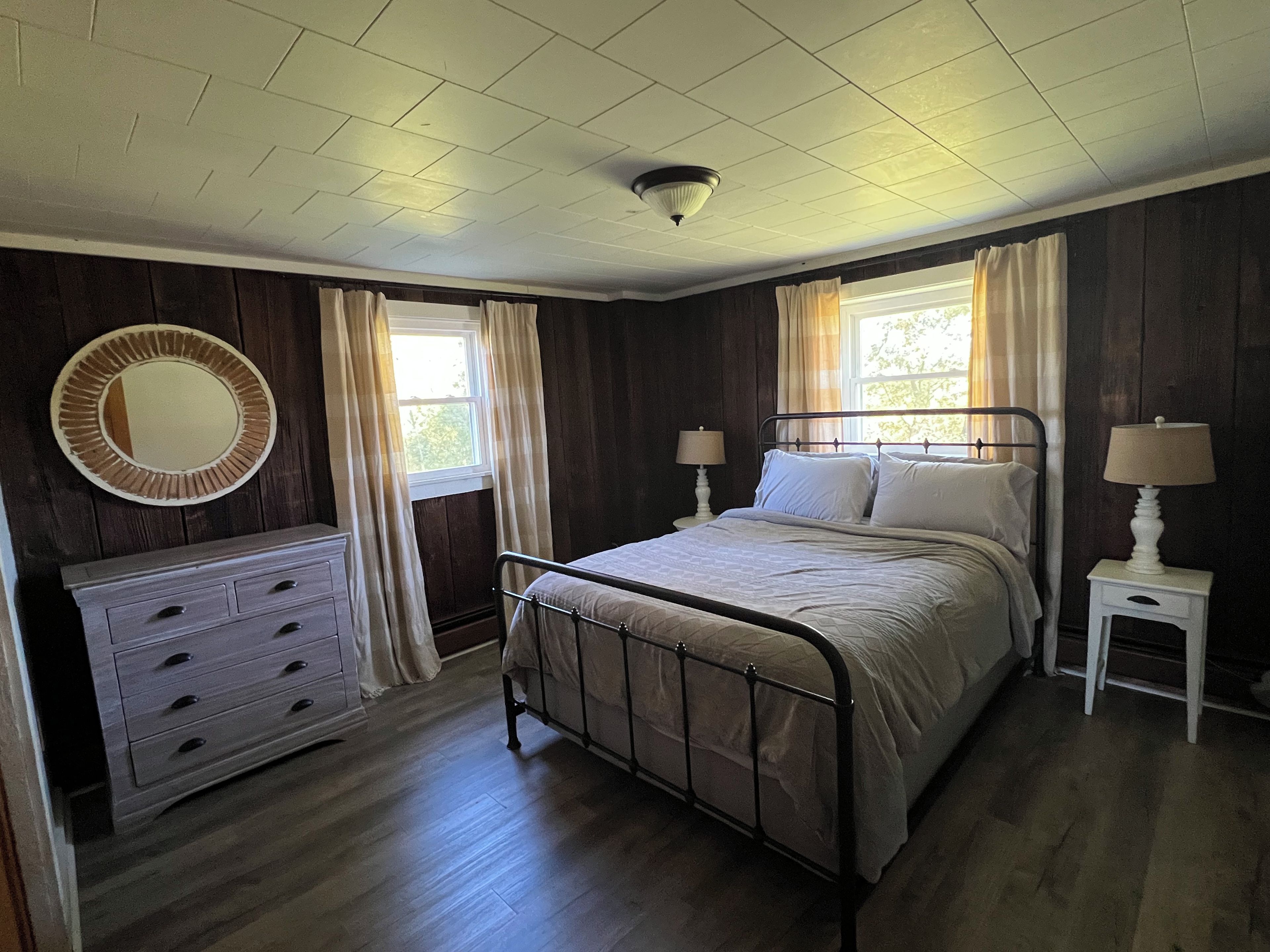 A bedroom with a bed, dresser, bedside tables, and a window with curtains.