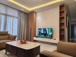 A modern living room with a flat-screen TV, a sofa, a coffee table, and a bookshelf. - Spacious 3BR Serviced Apartment Near Bole Airport (Addis Ababa)