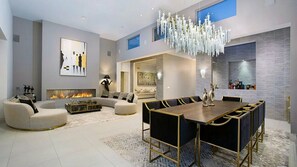 A modern living room with a fireplace, a dining area with a large table, and a chandelier. - Lemmer Grange (Los Angeles)