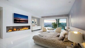 A modern bedroom with a fireplace, a large bed, a TV, and a view of the outdoors. - Lemmer Grange (Los Angeles)