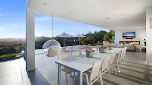 Un interior modern amb zona de menjador, una llar de foc i un gran finestral amb vista a una piscina i paisatge.