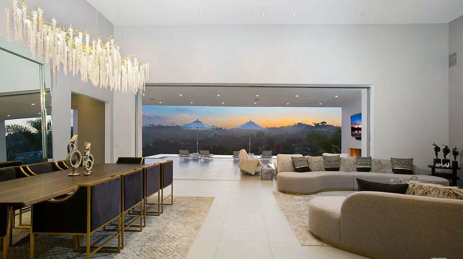 A modern living room with a large window overlooking a scenic view, a dining area with a long table, and a cozy seating arrangement.