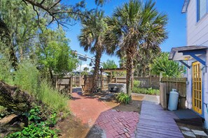 A backyard with a brick pathway, palm trees, a wooden deck, and a barbecue area. - 2BR Duplex · Sleeps 6 · Private Hot Tub · Dogs OK (Saint Augustine)